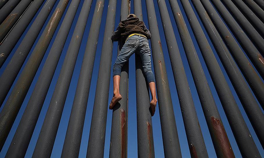 Тихуана, Мексика. Мигрант пытается забраться на стену между Мексикой и США