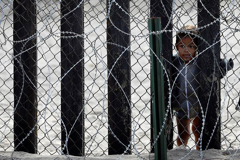 Сан-Диего, Калифорния. Мальчик смотрит через забор на границе Мексики и США 
