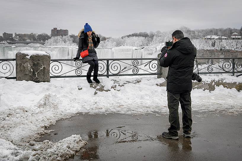 Туристы фотографируются на фоне замерзшего водопада