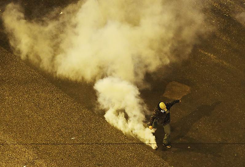 Участник акции протеста отбрасывает шашку со слезоточивым газом 