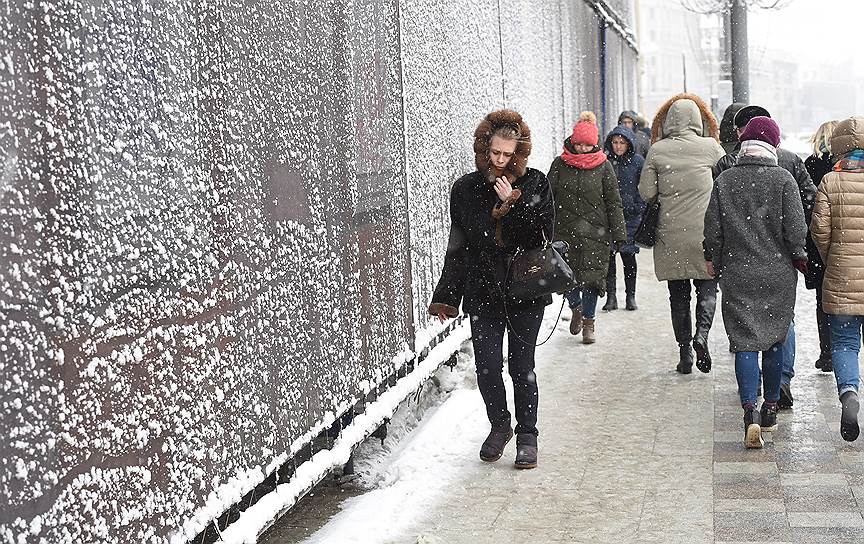 Прохожие идут по тротуару во время снегопада