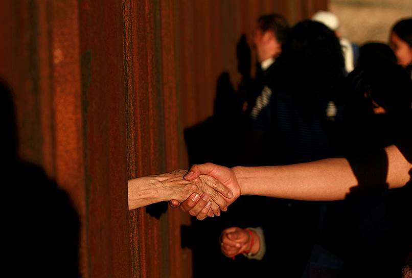 Сьюдад-Хуарес, Мексика. Люди пожимают друг другу руки через забор на границе с США