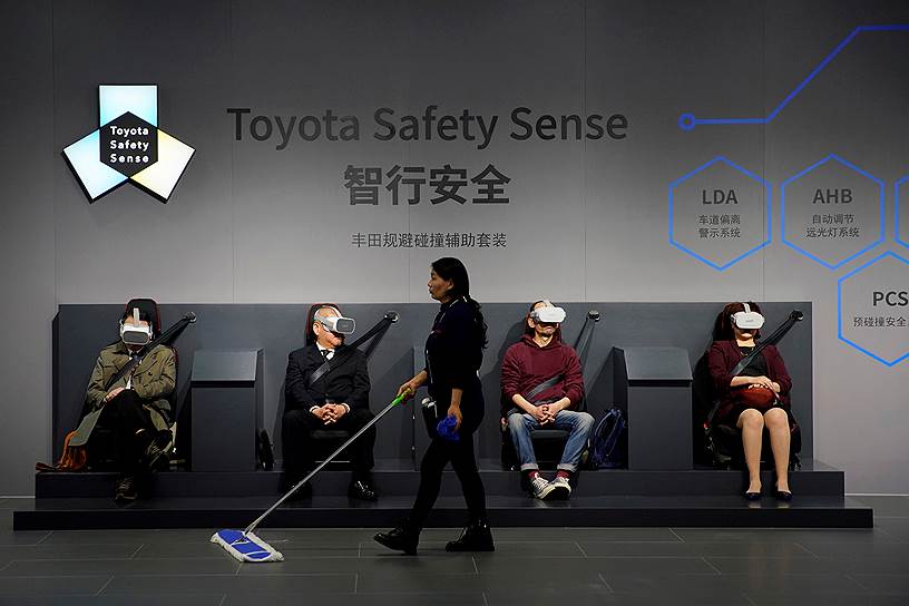 Шанхай. Китай. Уборщица проходит мимо посетителей Шанхайского автосалона, тестирующих с помощью VR-технологий систему предотвращения столкновений Toyota Safety Sense 