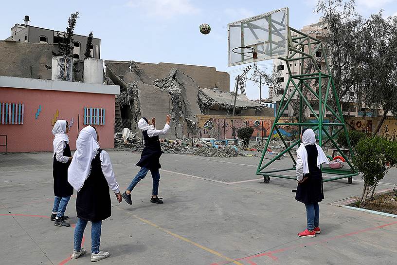 Газа, Палестина. Школьницы играют в баскетбол рядом с разрушенным в результате авиаударов зданием  