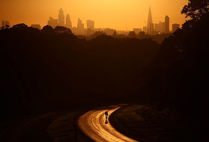 Лондон, Великобритания. Велосипедист едет к деловому кварталу во время восхода солнца