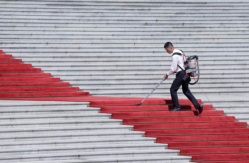 Пекин, Китай. Служащий очищает красную ковровую дорожку перед зданием парламента