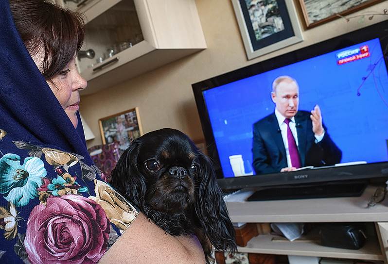 Женщина с собакой смотрит у себя дома прямую линию с Владимиром Путиным