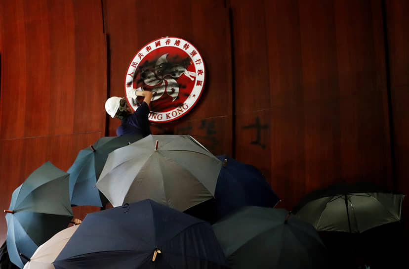 Гонконг, КНР. Один из протестующих закрашивает герб Гонконга в здании парламента