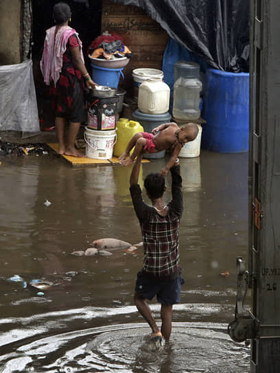 Мумбай, Индия. Мужчина несет ребенка на руках через затопленную из-за проливных дождей улицу