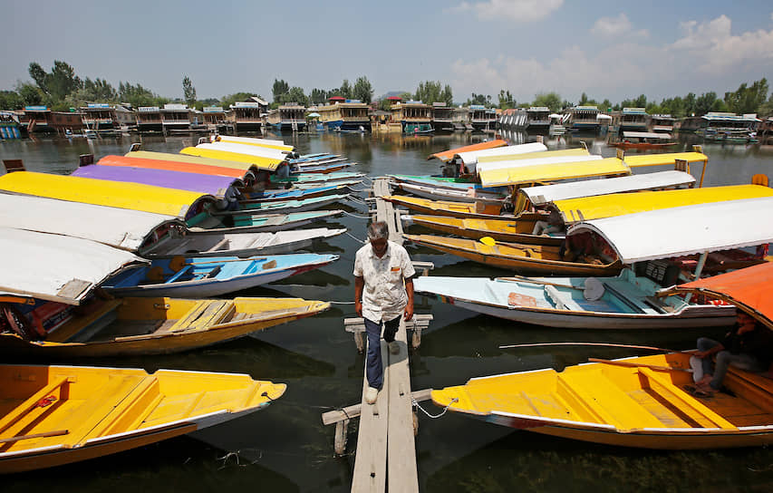 Сринагар, Индия. Мужчина идет мимо лодок для туристов на озере Дал