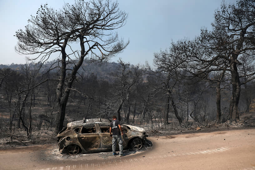 Эвия, Греция. Мужчина рядом с автомобилем, сгоревшем при лесном пожаре