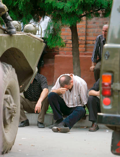Мужчина сидит на асфальте и плачет среди солдат, находящихся в оцеплении вокруг школы