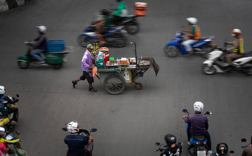 Бангкок, Таиланд. Уличный торговец толкает свою тележку на оживленном перекрестке