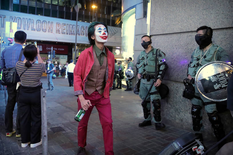 Гонконг, Китай. Мужчина в костюме Джокера проходит мимо полицейских