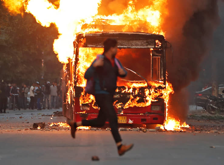 Нью-Дели, Индия. Участник акции протеста бежит около горящего автобуса