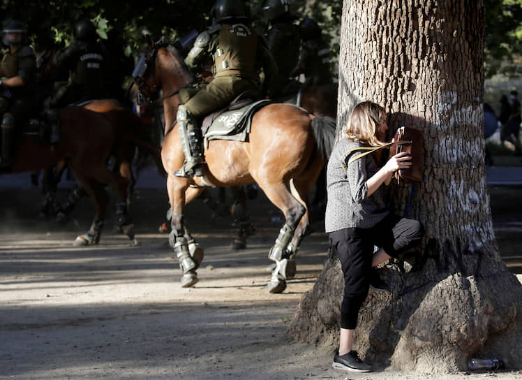 Сантьяго, Чили. Женщина прячется за деревом во время антиправительственных акций протеста 