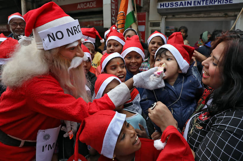 Калькутта, Индия. Мужчина в костюме Санта-Клауса кормит ребенка пирогом 