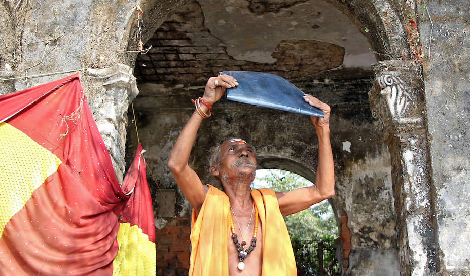 Агартала, Индия. Индуистский священник наблюдает солнечное затмение возле храма