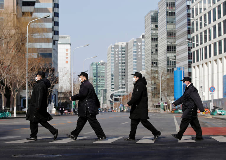 Пекин, Китай. Сотрудники службы безопасности в масках переходят через дорогу