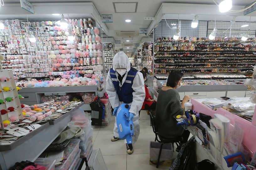 Рабочий в защитном костюме распыляет дезинфектант в магазине Сеула, Южная Корея