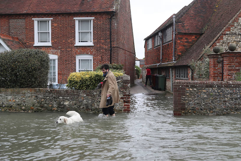 Мужчина гуляет с собакой на затопленной улице в английском графстве Суссекс 