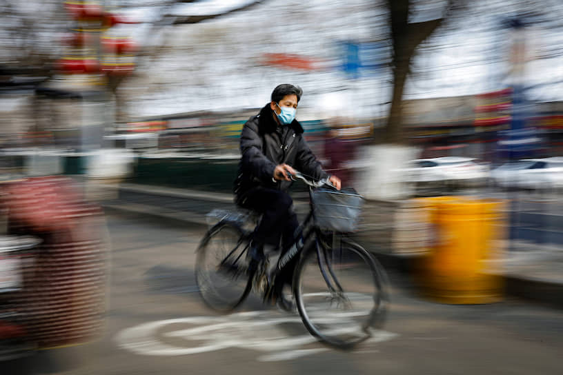 Пекин, Китай. Мужчина в медицинской маске едет на велосипеде