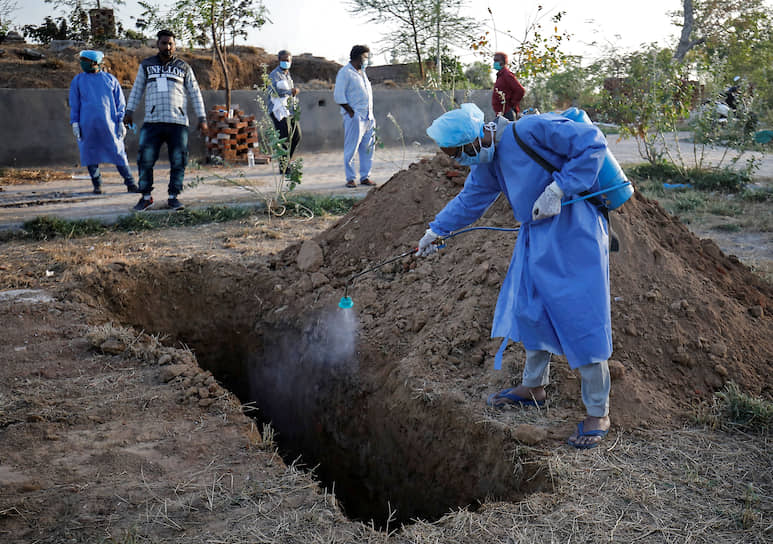 Индия. Муниципальный служащий в защитном костюме распыляет дезинфицирующий раствор в могиле перед захоронением женщины, умершей от коронавируса