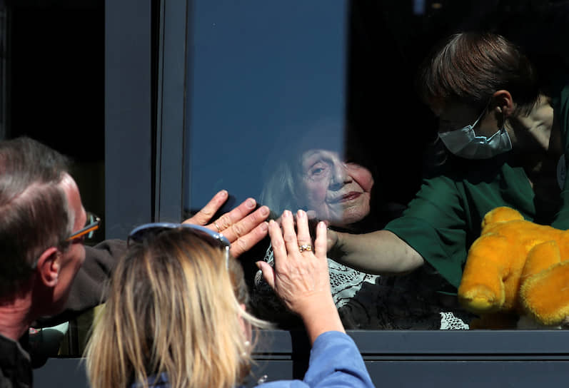 Брюссель, Бельгия. Находящаяся на карантине 92-летняя женщина здоровается со своими детьми через стекло