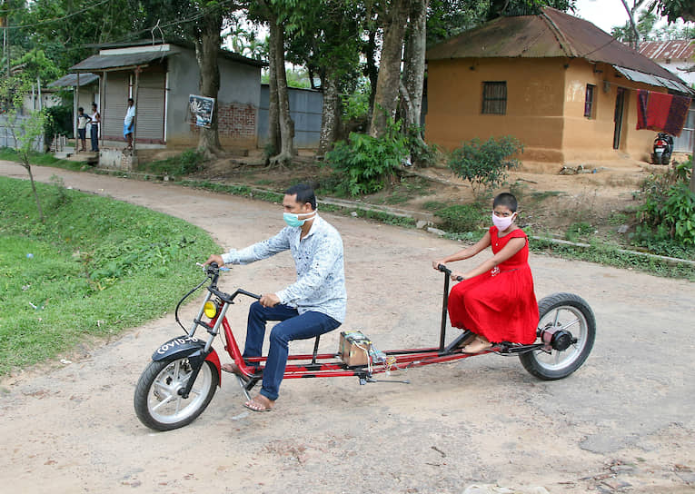 Инженер Партха Саха и его дочь Прагья Саха катаются на модифицированном велосипеде с батарейным питанием, который он разработал для социального дистанцирования