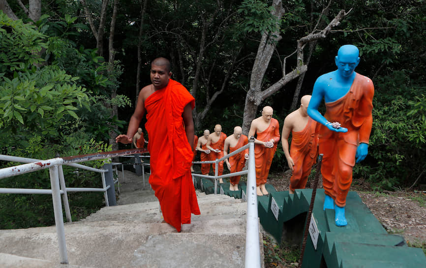 Коломбо, Шри-Ланка. Буддийский монах идет мимо храмовых статуй во время комендантского часа 