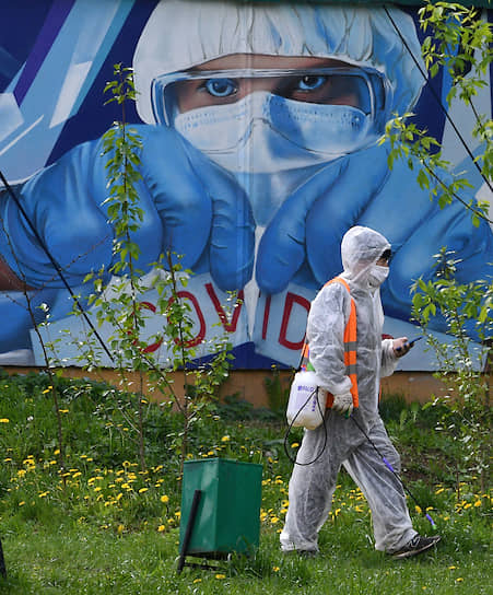 Москва. Сотрудник службы дезинфекции во дворе на фоне изображения врача на стене