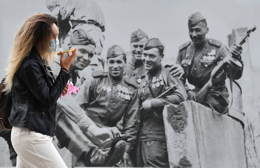 12 мая. Москва. Девушка в медицинской маске идет мимо плаката ко Дню Победы в первый день введения обязательного ношения масок и перчаток в общественных местах