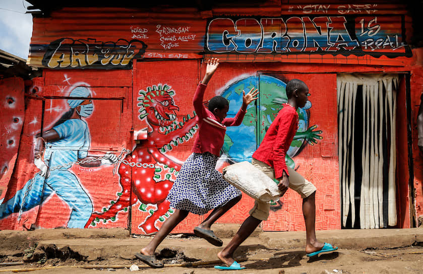 Найроби, Кения. Дети бегут по улице мимо граффити, предупреждающего об опасности коронавируса