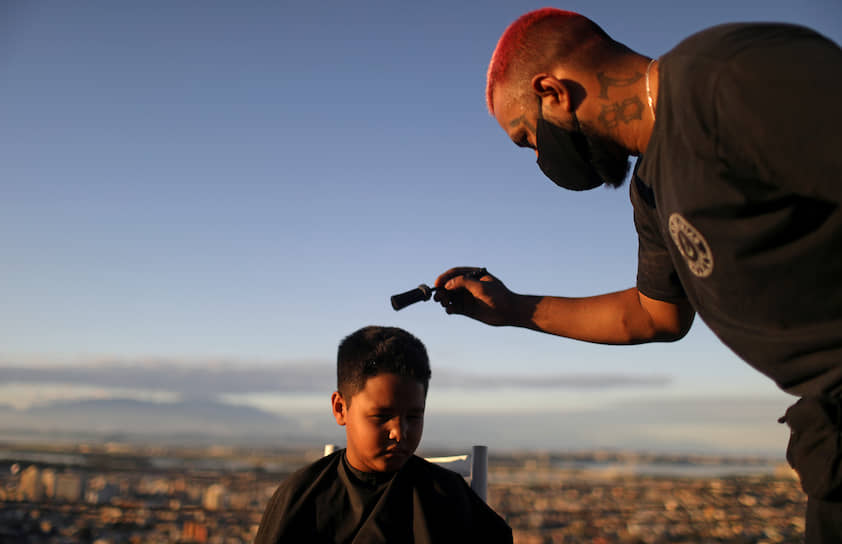 Рио-де-Жанейро, Бразилия. Парикмахер стрижет ребенка, пока его место работы закрыто из-за коронавируса 