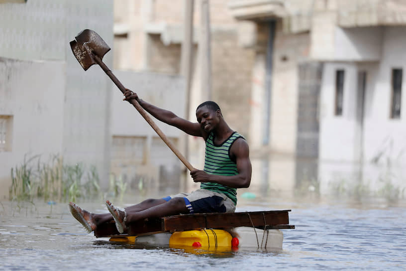 Кер Массар, Сенегал. Мужчина использует лопату для гребли на самодельном плоту по затопленным улицам 