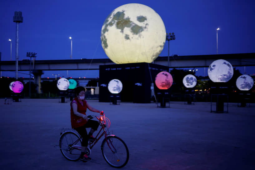 Сеул, Южная Корея. Женщина едет на велосипеде мимо лунной инсталляции, посвященной традиционному осеннему празднику Чхусок
