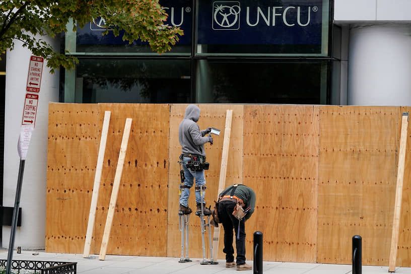 Рабочие заколачивают фанерой витрину магазина в Вашингтоне