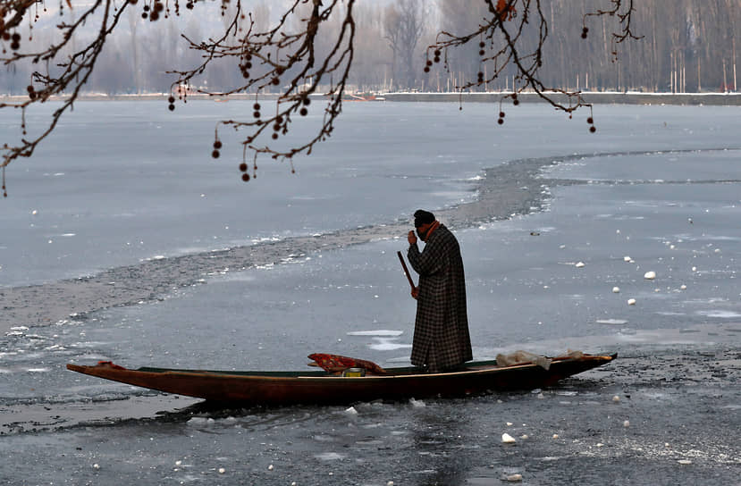 Сринагар, Индия. Мужчина плывет на лодке по частично замерзшему озеру