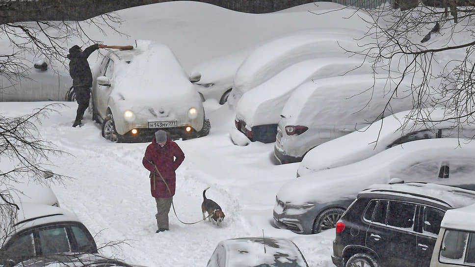 Водитель чистит автомобиль от снега