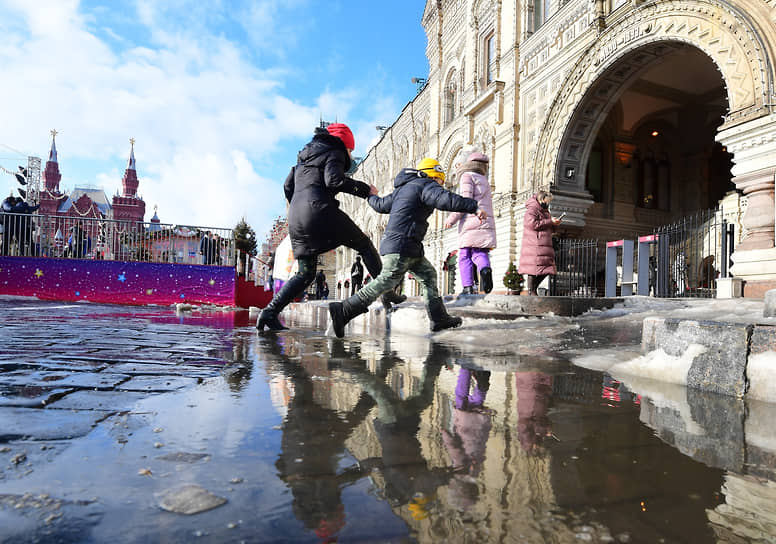 Москва, Россия. Люди перепрыгивают лужу возле здания ГУМа