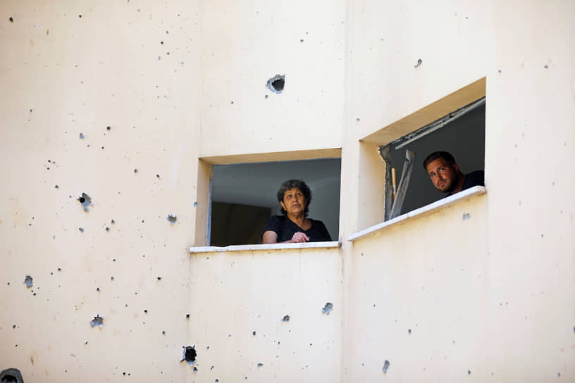 Люди выглядывают из окон здания, поврежденного ударом ракеты из Газы, в Петах-Тиква (Израиль)