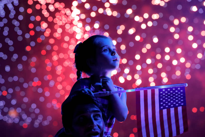 Нью-Йорк, США. Ребенок держит флаг Соединенных Штатов во время фейерверка в честь Дня независимости