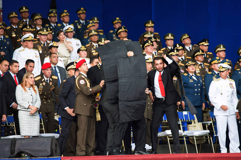 Охранники закрыли президента Венесуэлы Николаса Мадуро защитной экипировкой после того, как его атаковала группа начиненных взрывчаткой беспилотников, 2018 год