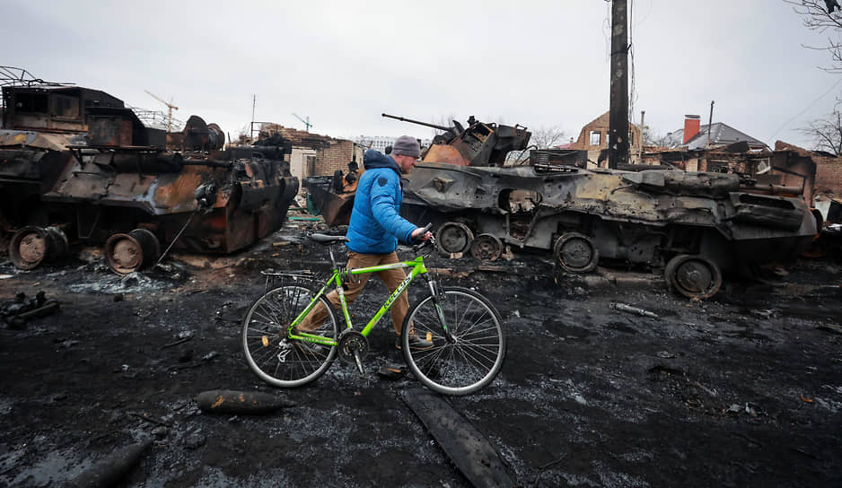 Мужчина с велосипедом проходит мимо сгоревшей военной техники