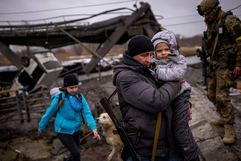 Мужчина помогает семье перейти через разрушенный мост на окраине Киева