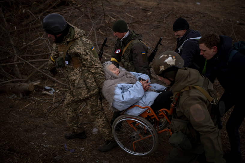 Украинские военные несут женщину в инвалидном кресле на окраине Киева