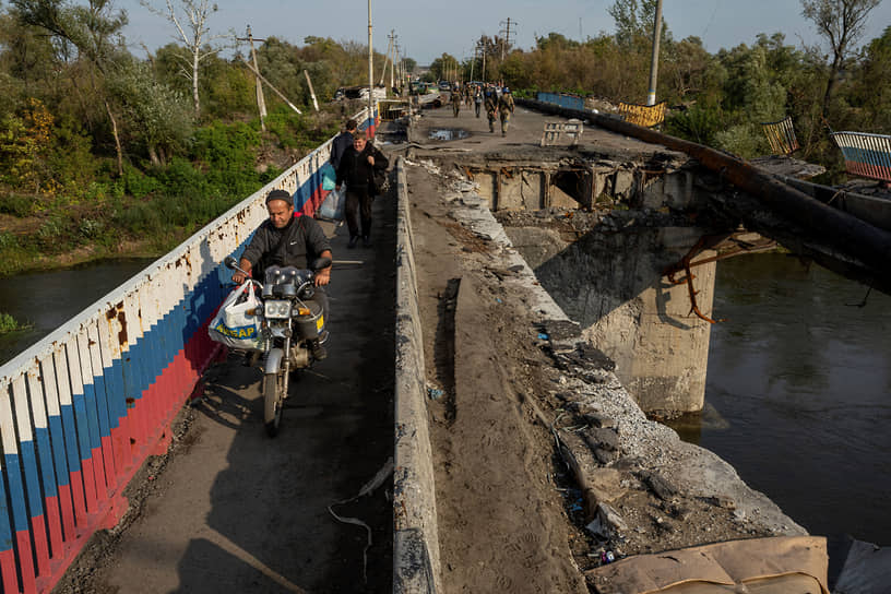 Мужчина едет на мотоцикле по разрушенному мосту через реку Оскол близ Купянска