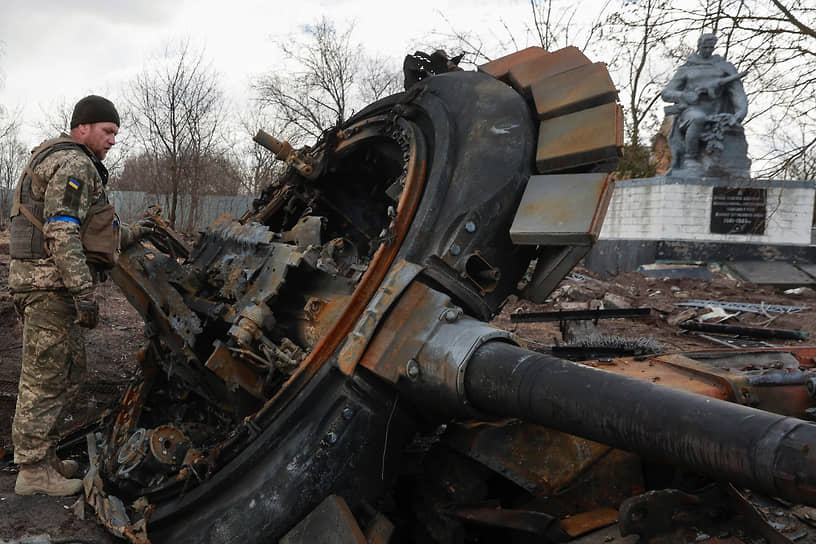 Украинский военнослужащий осматривает сгоревший танк в селе Лукьяновка Киевской области
