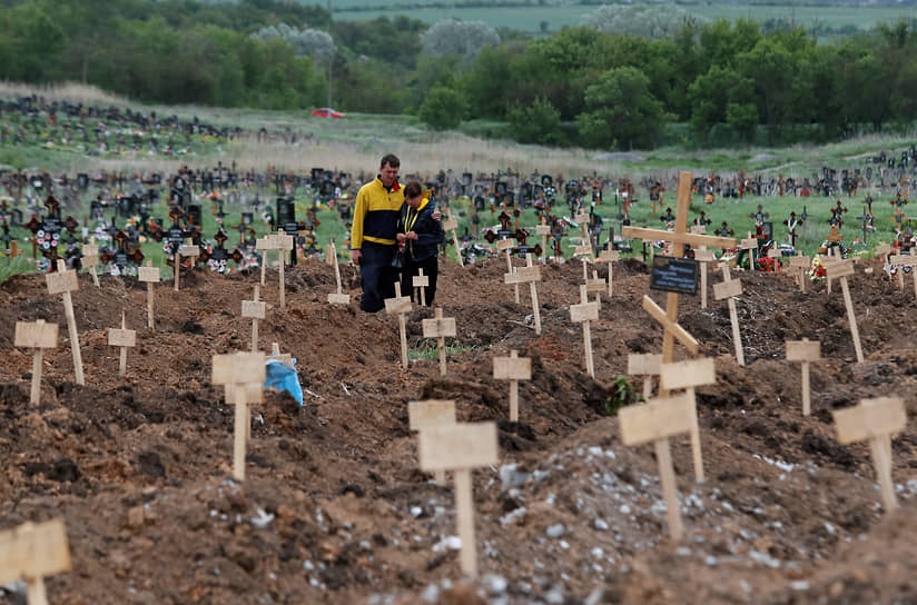 Люди среди свежевырытых могил в поселке Старый Крым около Мариуполя