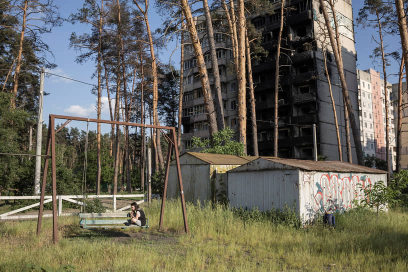 Женщина сидит на качелях рядом с разрушенным домом в Ирпене под Киевом